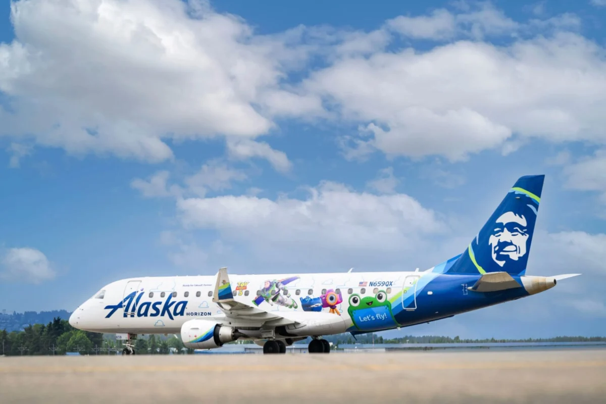 Alaska Horizon passenger plane with colorful character themed livery on the runway blue sky and tail with a smiling mascot logo