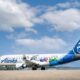 Alaska Horizon passenger plane with colorful character themed livery on the runway blue sky and tail with a smiling mascot logo