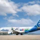 Alaska Horizon passenger plane with colorful character themed livery on the runway blue sky and tail with a smiling mascot logo