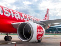 AirAsia aircraft on tarmac with large red fuselage and engine in foreground at an airport gate area