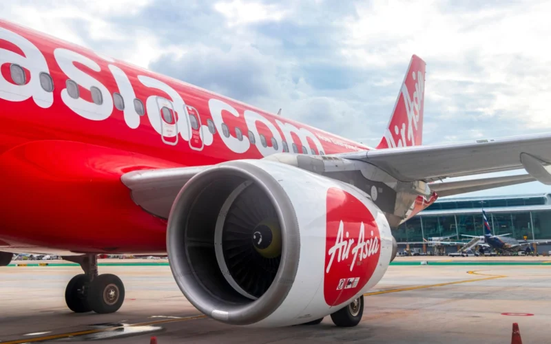 AirAsia aircraft on tarmac with large red fuselage and engine in foreground at an airport gate area