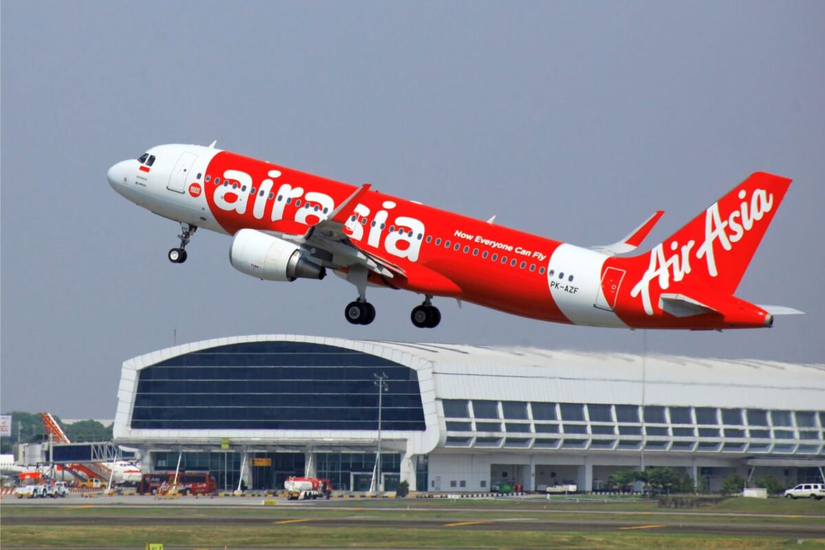 AirAsia red passenger jet lifting off the runway near terminal showing Now Everyone Can Fly slogan on fuselage