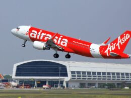 AirAsia red passenger jet lifting off the runway near terminal showing Now Everyone Can Fly slogan on fuselage
