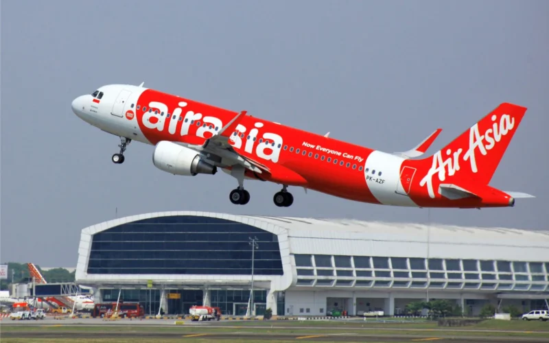 AirAsia red passenger jet lifting off the runway near terminal showing Now Everyone Can Fly slogan on fuselage