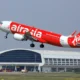 AirAsia red passenger jet lifting off the runway near terminal showing Now Everyone Can Fly slogan on fuselage