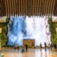 Indoor atrium with a large waterfall feature at the far end surrounded by plants and visitors walking around