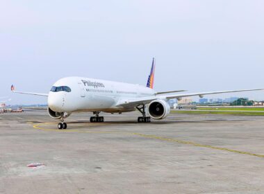 White Philippines airliner parked on the taxiway with a colorful tail design in the background on a sunny day at the airport.