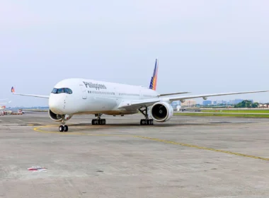 White Philippines airliner parked on the taxiway with a colorful tail design in the background on a sunny day at the airport.