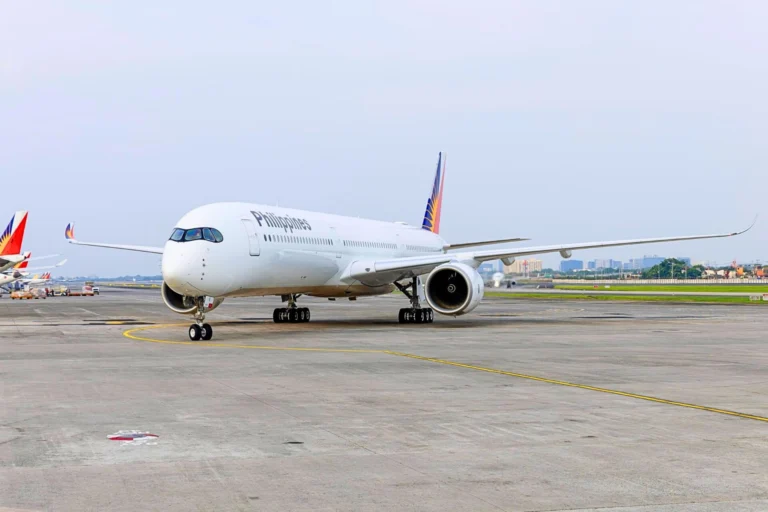 White Philippines airliner parked on the taxiway with a colorful tail design in the background on a sunny day at the airport