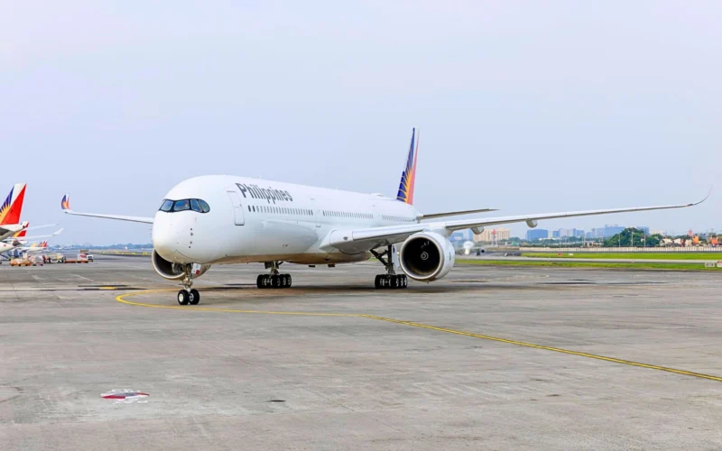 White Philippines airliner parked on the taxiway with a colorful tail design in the background on a sunny day at the airport