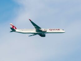 Qatar Airways wide body jet in flight with red tail logo flying against a clear blue sky