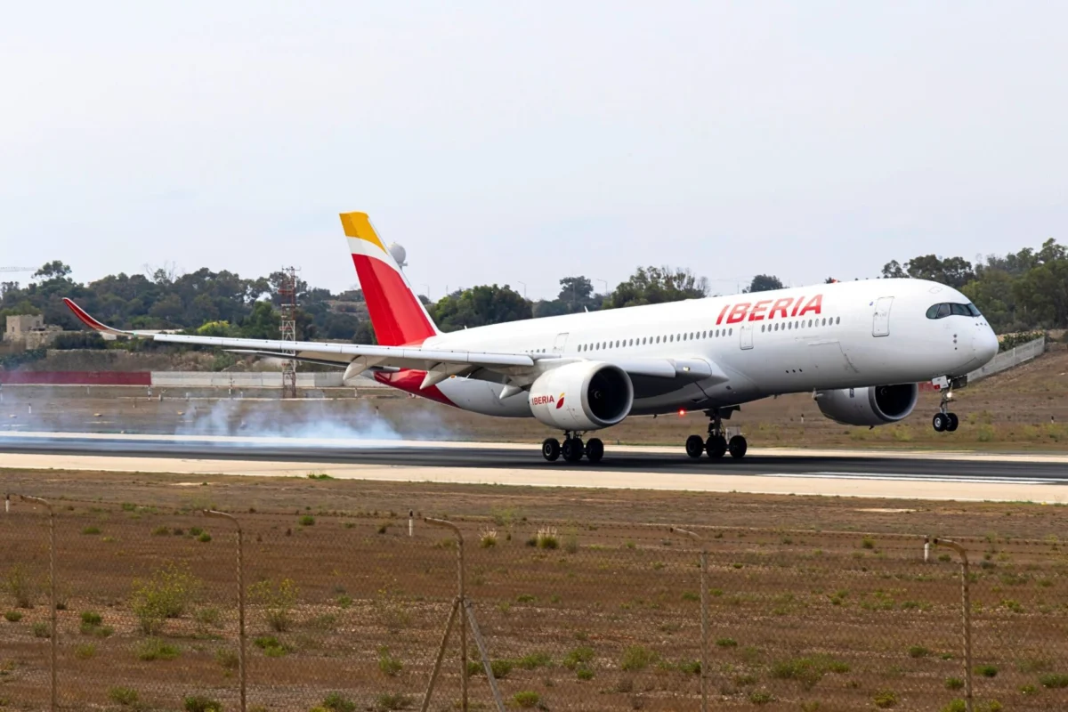 Iberia narrow body airplane on a runway with ground smoke tail fin in yellow and red preparing for takeoff or landing roll