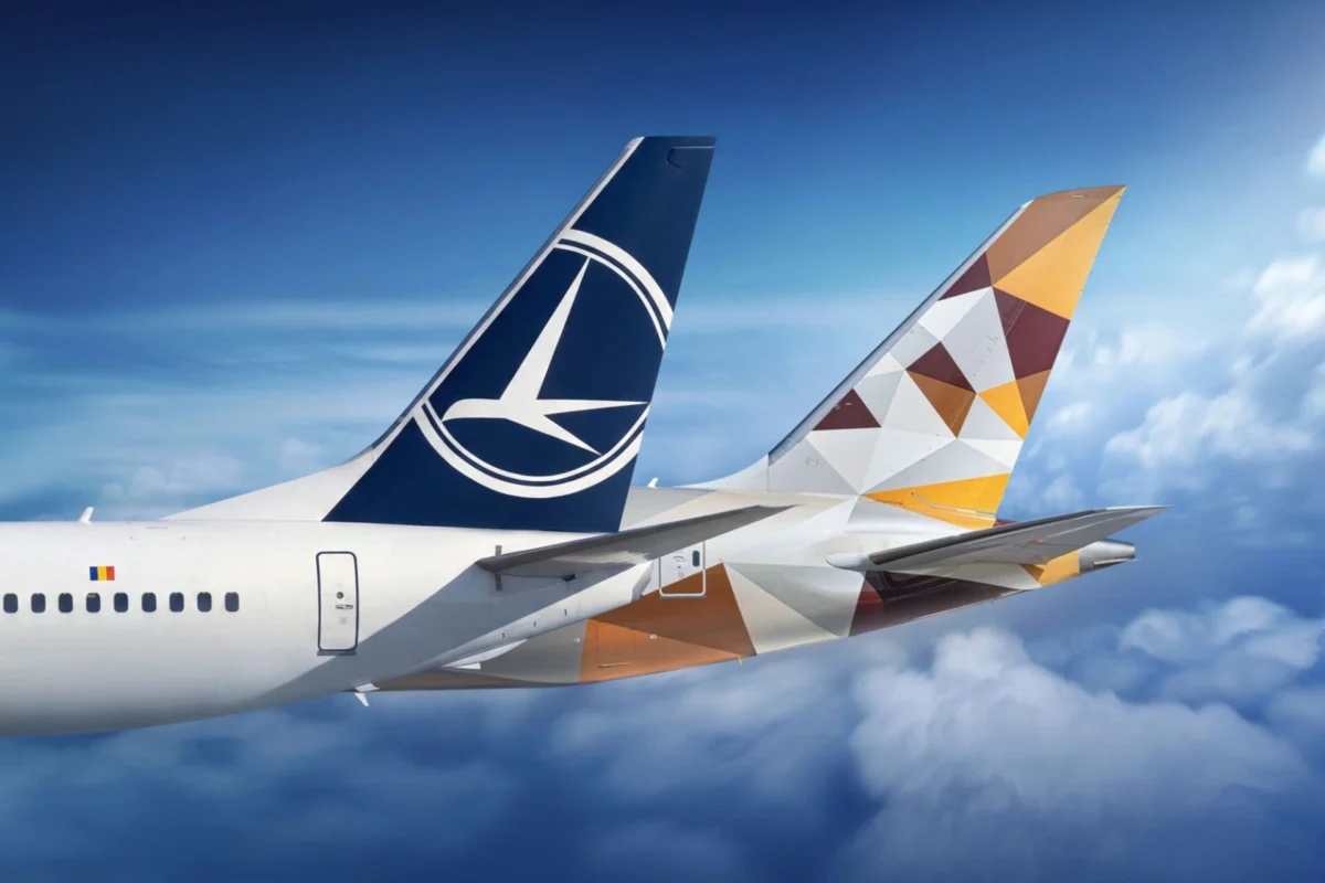 Two commercial aircraft tails in flight one with a blue Lufthansa logo the other with a geometric orange brown pattern against a blue sky