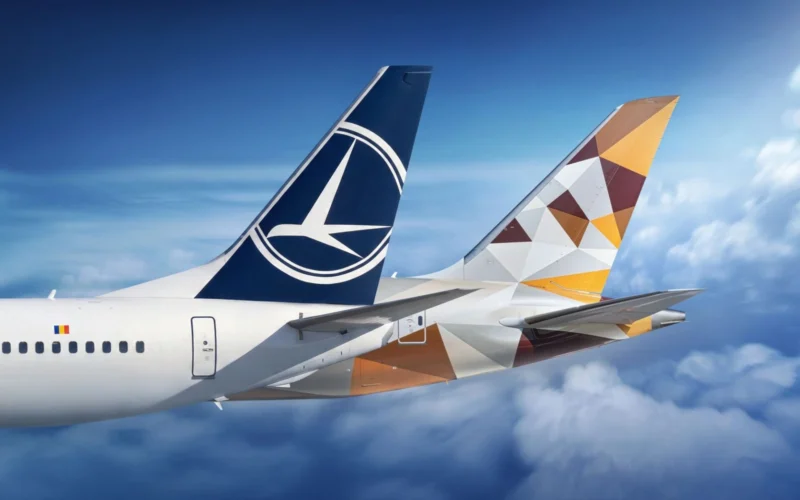 Two commercial aircraft tails in flight one with a blue Lufthansa logo the other with a geometric orange brown pattern against a blue sky