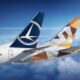 Two commercial aircraft tails in flight one with a blue Lufthansa logo the other with a geometric orange brown pattern against a blue sky