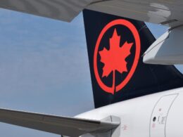 Rear of an Air Canada airplane with a black tail featuring a bright red maple leaf logo a wing in the foreground