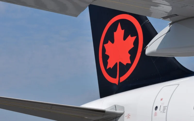 Rear of an Air Canada airplane with a black tail featuring a bright red maple leaf logo a wing in the foreground