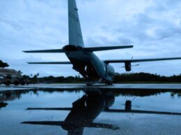 Rear view of a military transport aircraft C 130 on a runway wings spread reflected in a wet surface