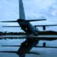 Rear view of a military transport aircraft C 130 on a runway wings spread reflected in a wet surface