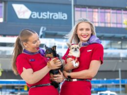 Two women in red uniforms holding small dogs outdoors in front of a building with a visible Australia sign in the background