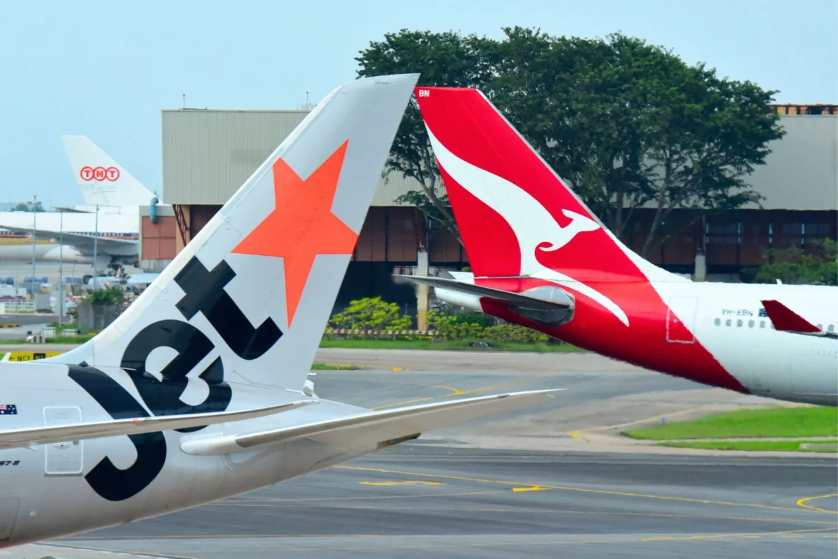 Qantas and Jetstar announce Western Sydney Airport flights Two airplane tails at an airport one with an orange star design and the other red with a white kangaroo logo parked near a hangar