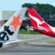 Two airplane tails at an airport one with an orange star design and the other red with a white kangaroo logo parked near a hangar