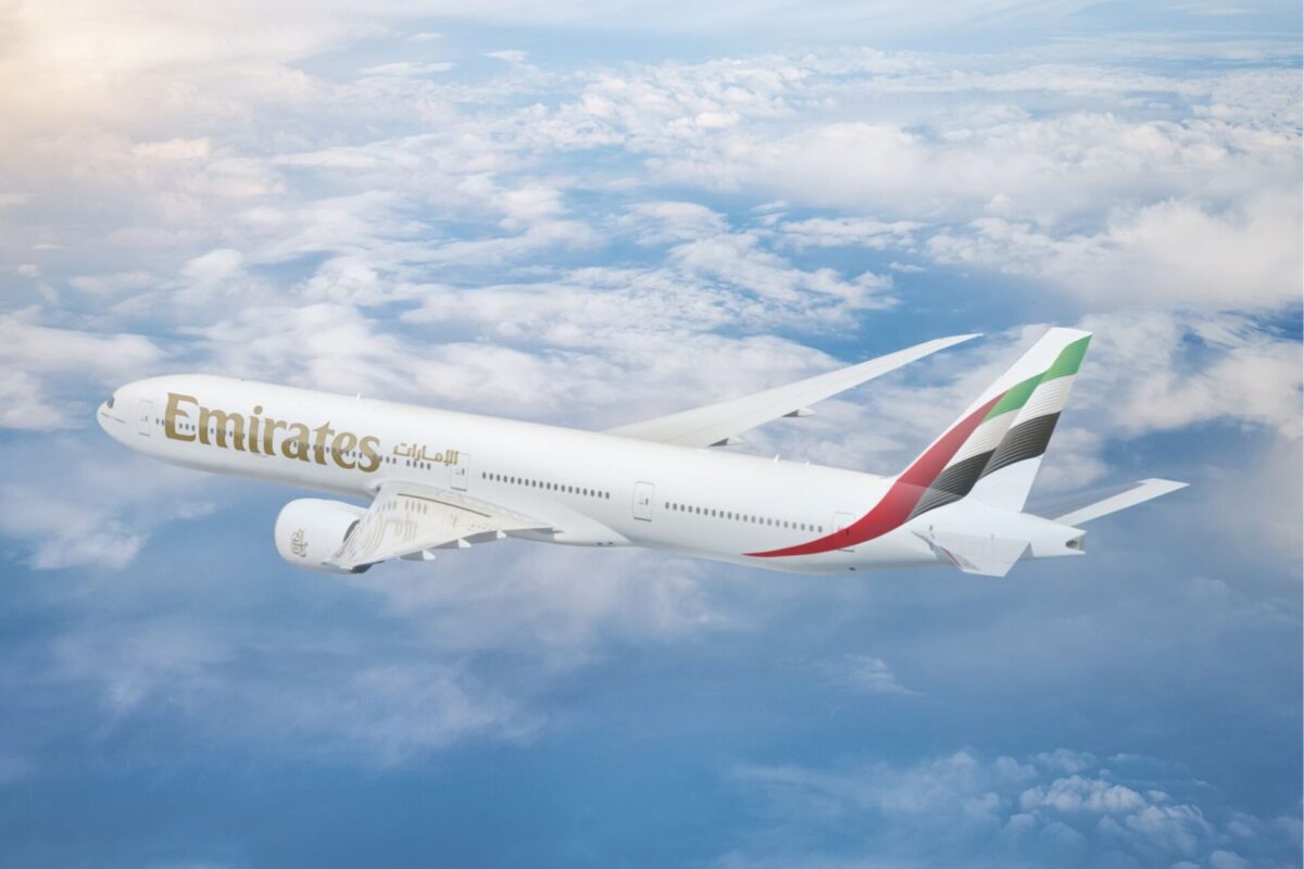 Emirates passenger jet flying above fluffy clouds under a blue sky with its wing visible