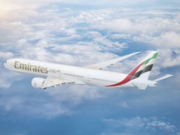 Emirates passenger jet flying above fluffy clouds under a blue sky with its wing visible