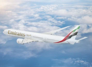Emirates passenger jet flying above fluffy clouds under a blue sky with its wing visible