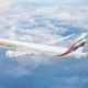 Emirates passenger jet flying above fluffy clouds under a blue sky with its wing visible