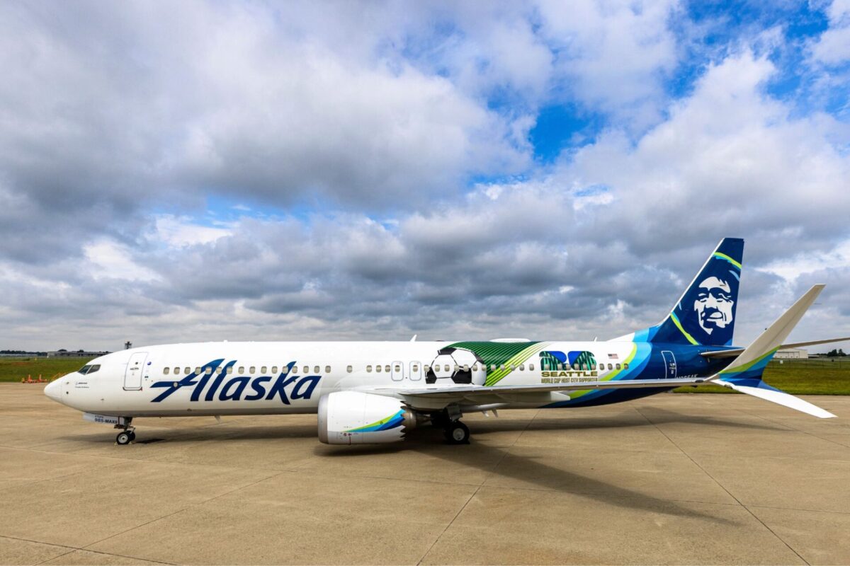 White Alaska Airlines jet on the tarmac with a colorful Seattle World Cup City liverie and tail art under a cloudy sky