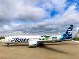 White Alaska Airlines jet on the tarmac with a colorful Seattle World Cup City liverie and tail art under a cloudy sky