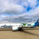 White Alaska Airlines jet on the tarmac with a colorful Seattle World Cup City liverie and tail art under a cloudy sky