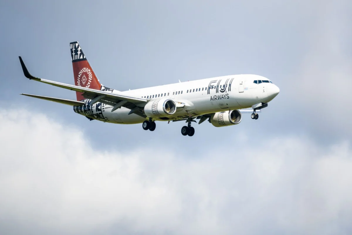 White passenger jet with red tail and bold logo on fuselage flying in cloudy blue sky