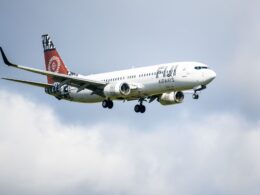 White passenger jet with red tail and bold logo on fuselage flying in cloudy blue sky