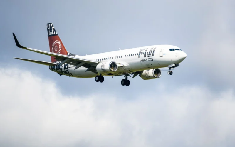 White passenger jet with red tail and bold logo on fuselage flying in cloudy blue sky