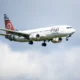 White passenger jet with red tail and bold logo on fuselage flying in cloudy blue sky