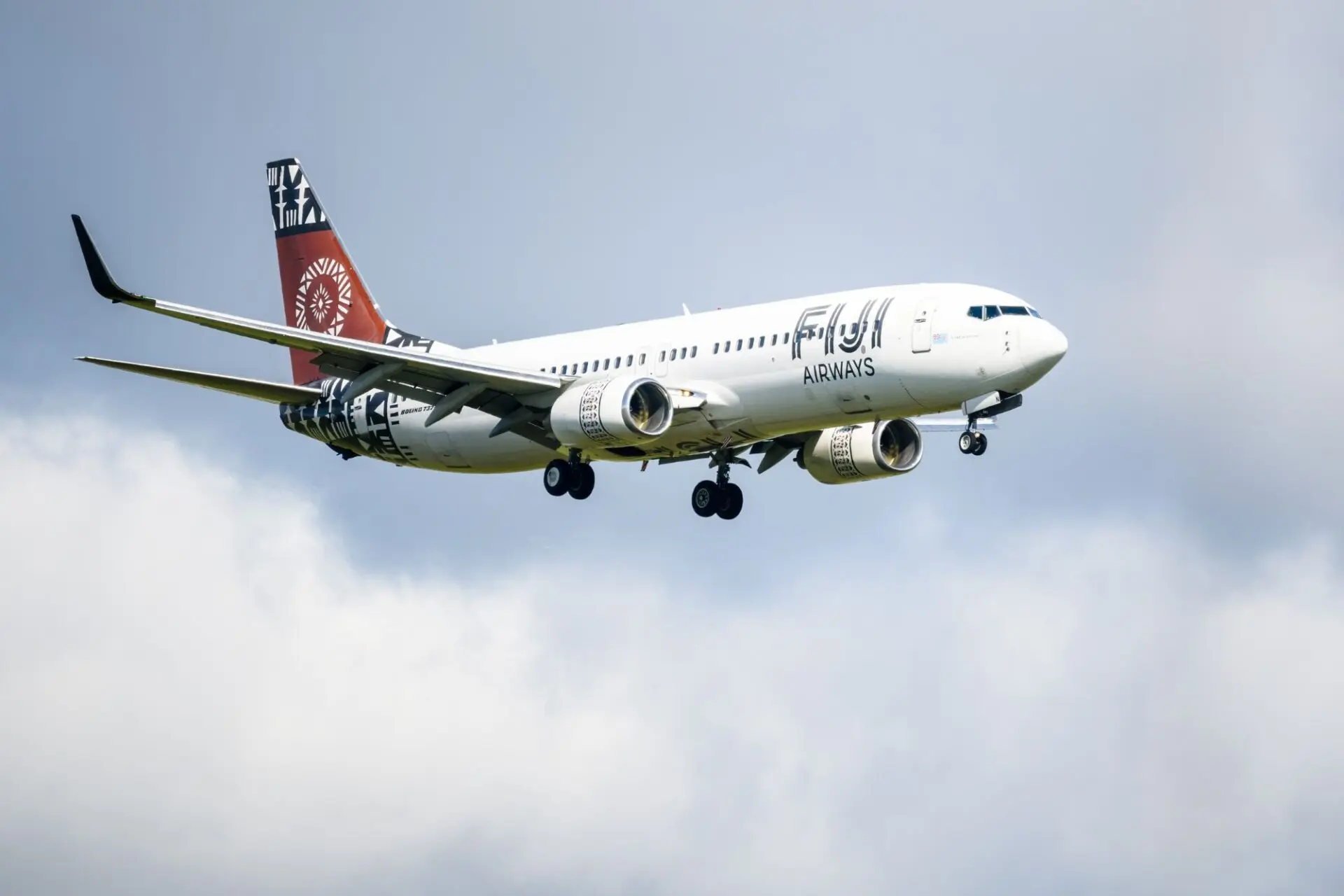 White passenger jet with red tail and bold logo on fuselage flying in cloudy blue sky