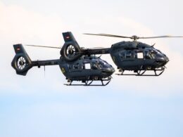 Two dark gray military helicopters flying side by side against a blue sky