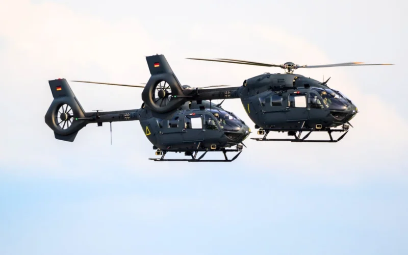 Two dark gray military helicopters flying side by side against a blue sky