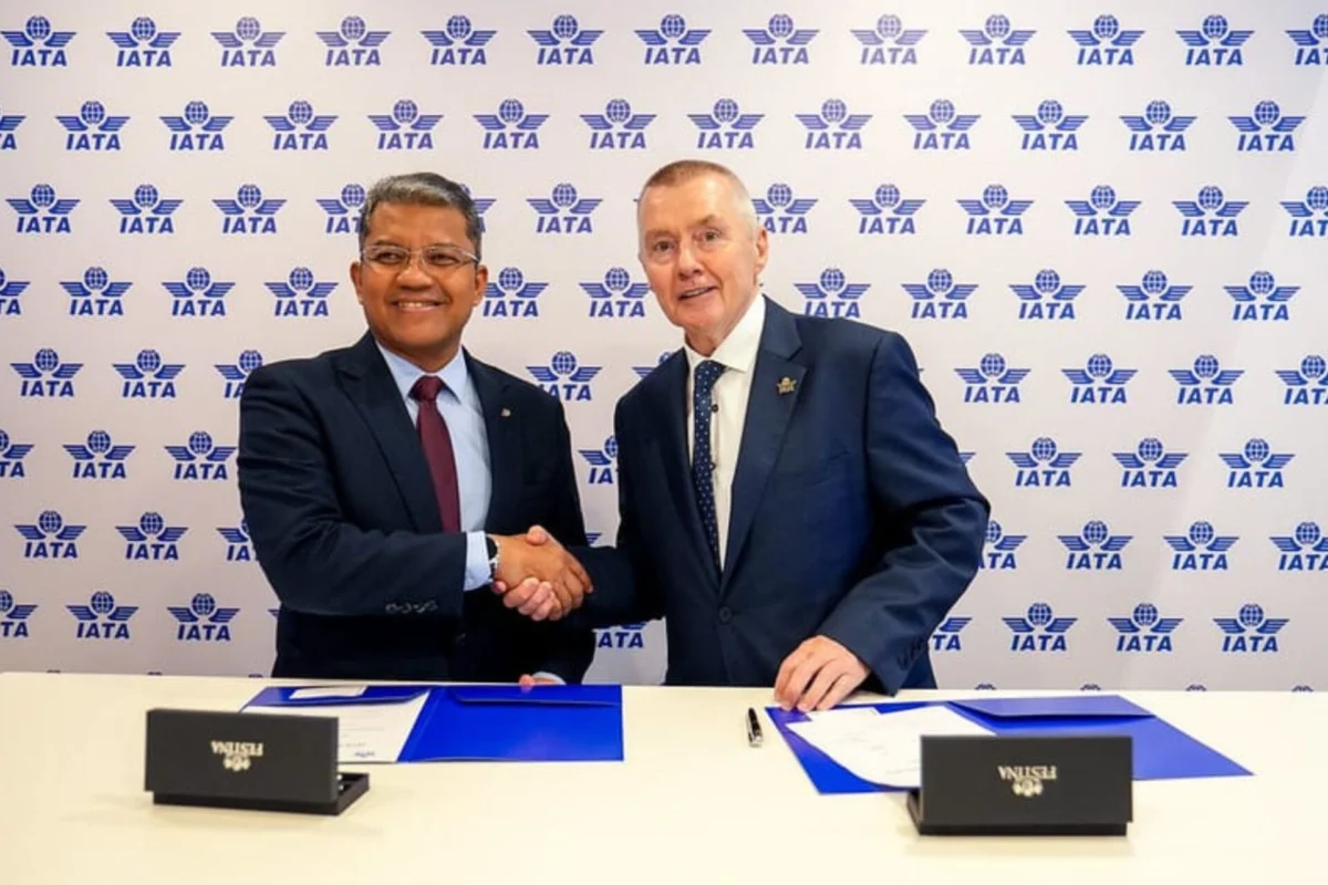Two men in suits shake hands at a signing ceremony against an IATA backdrop with documents on the table behind them