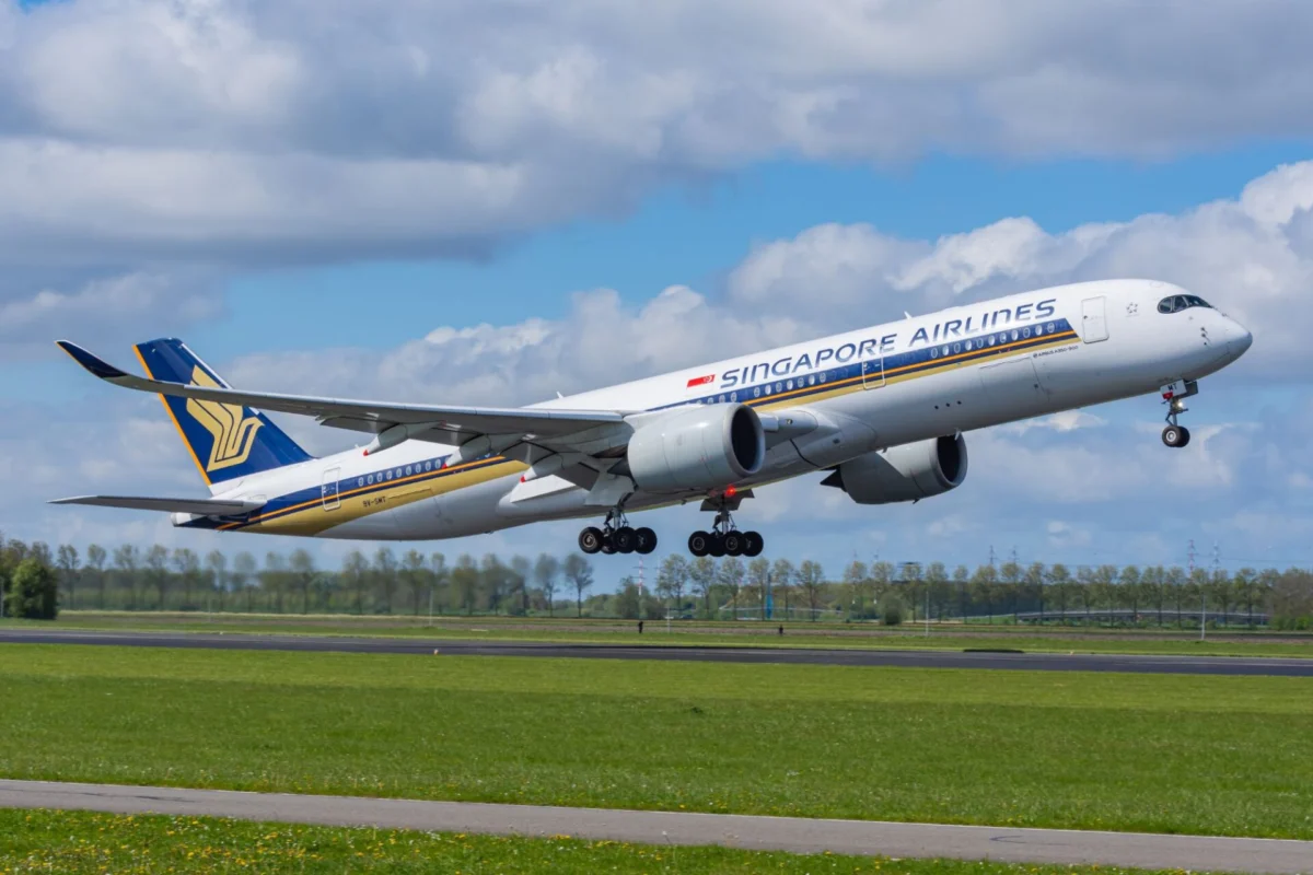 Singapore Airlines passenger jet lifting off the runway wheels still extended under a partly cloudy blue sky