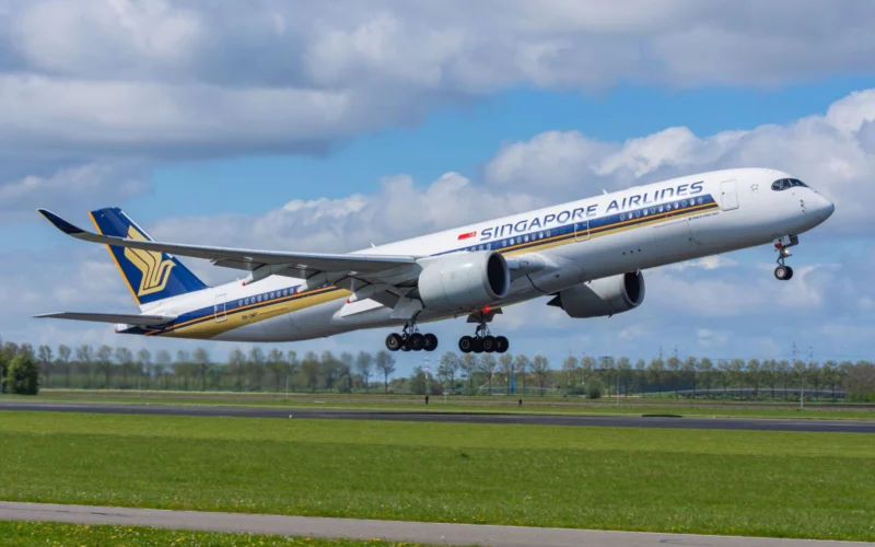 Singapore Airlines passenger jet lifting off the runway wheels still extended under a partly cloudy blue sky