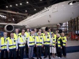 Group of airline staff in yellow safety vests posing in a hangar with a large white plane behind them