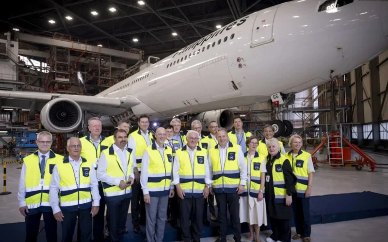 Group of airline staff in yellow safety vests posing in a hangar with a large white plane behind them