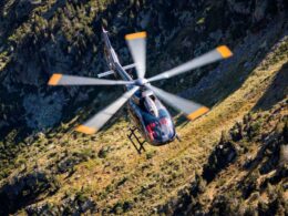 A helicopter flying over a rocky mountain landscape viewed from above with spinning rotors and a grassy valley below during daylight