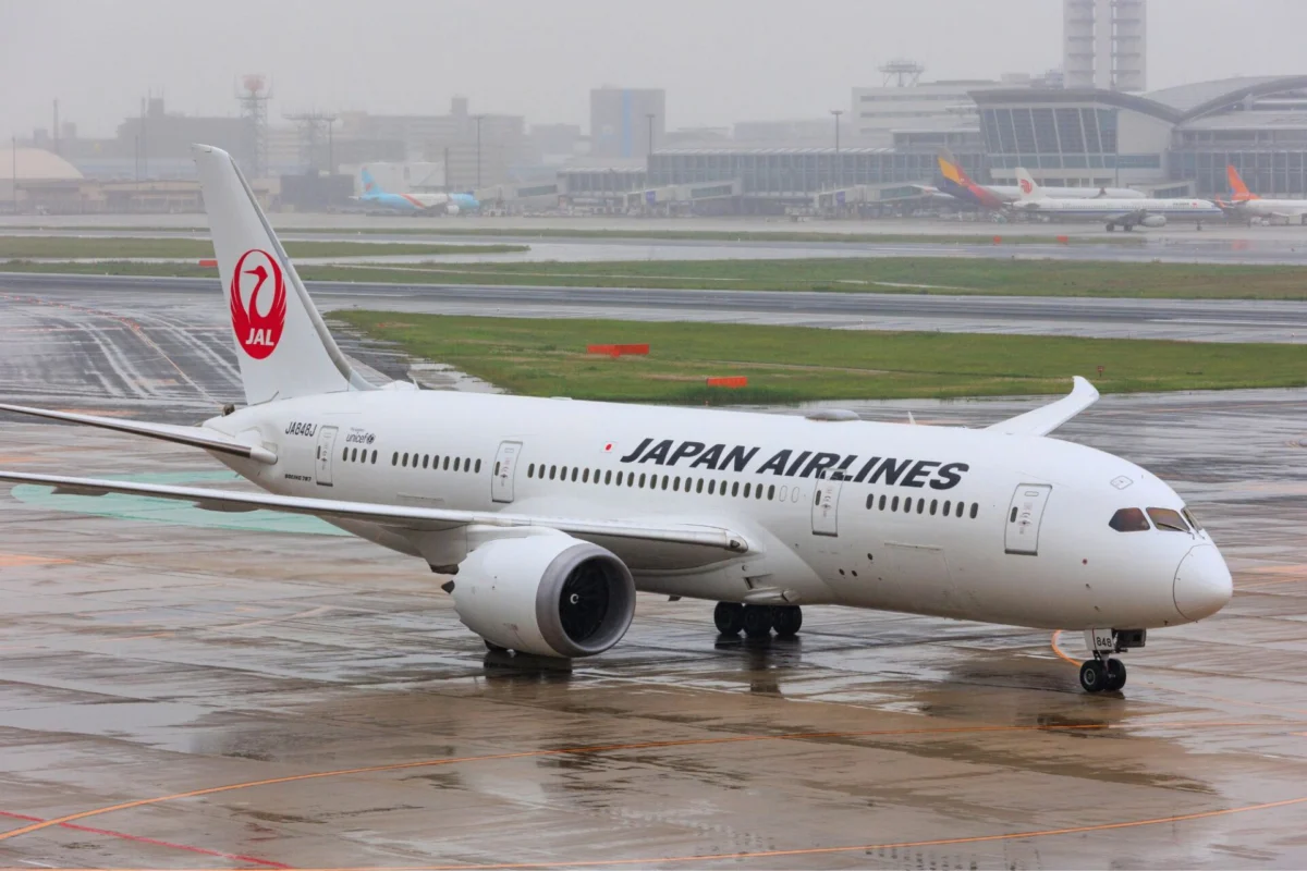 JAL executives face pay cuts after crew alcohol incident Front half of a Japan Airlines plane on a wet tarmac with a red JAL tail logo and airport buildings in the rainy background