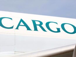 Close up of a white cargo aircraft fuselage with large turquoise letters spelling CARGO against a blue sky