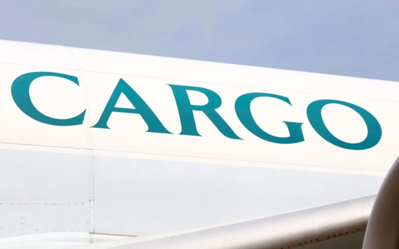 Close up of a white cargo aircraft fuselage with large turquoise letters spelling CARGO against a blue sky