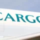 Close up of a white cargo aircraft fuselage with large turquoise letters spelling CARGO against a blue sky